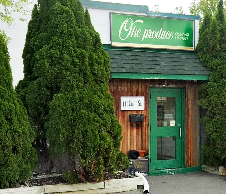 Photo of Oke Produce's storefront. A green door on a wooden building, surrounded by trees